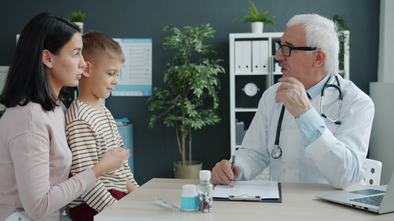 Doctor talking to mother and child at desk, group health